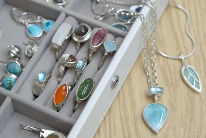 Close up of a jewllery box with visible hand-made jewellery including rings and necklaces with inset gemstones.
