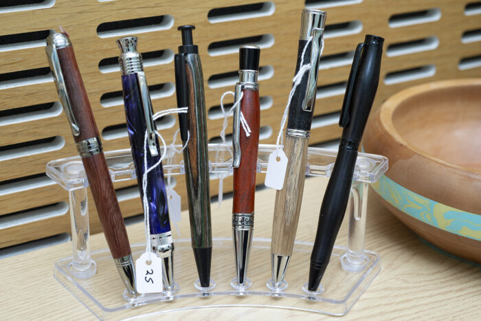Six hand-made pens created via wood-turning displayed on a stand.
